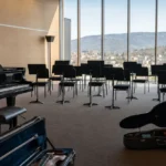 Salle de répétition vide, piano et pupitres face aux collines jurassiennes